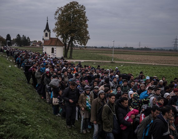 Migrants walking past a church, escorted by Slovenian riot police to a registration camp outside Dobova, Slovenia. The small Balkan nations along the path of the human migration through Europe have seen record numbers of refugees cross their borders, and have been overwhelmed in their ability to manage the human flow (Sergey Ponomarev, The New York Times - October 22, 2015).